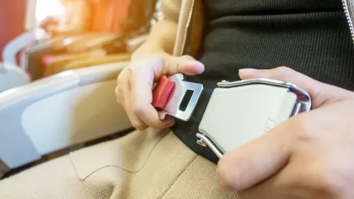 راكب في الطائرة يقوم بربط حزام الأمان حول خصره، مما يعكس تحديات الراحة أثناء الرحلات الجوية الطويلة.