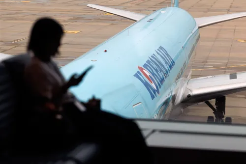 امرأة تجلس في مطار، تركز على هاتفها، بينما تظهر طائرة الخطوط الجوية الكورية في الخلفية، مما يعكس الاستثمارات الكبيرة في الطيران.