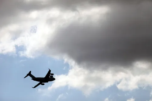 طائرة عسكرية تحلق في السماء مع سحب داكنة، تعكس جهود إدارة ترامب لترحيل المهاجرين إلى بلدان ثالثة.