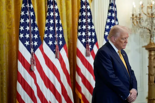 ترامب يقف بجوار أعلام الولايات المتحدة في غرفة رسمية، معبرًا عن التركيز على القضايا الدينية في مكان العمل الفيدرالي.