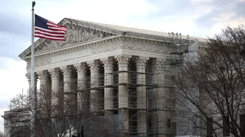 مبنى المحكمة العليا الأمريكية مع أعمدة بارزة وعلم الولايات المتحدة يرفرف، بينما يتم تنفيذ أعمال صيانة خارجية.