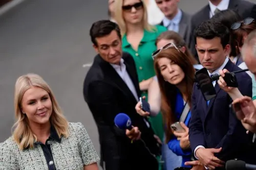 مراسلة صحفية تتحدث أمام مجموعة من الصحفيين، في خلفية مشهد يعكس التوترات حول تغطية إدارة ترامب للأخبار.