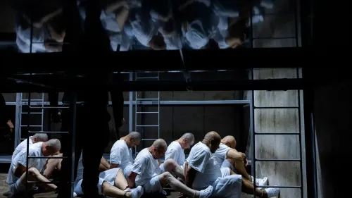 مجموعة من المعتقلين في ملابس بيضاء يجلسون معًا في مركز احتجاز مظلم، مما يعكس الظروف القاسية التي يواجهها المحتجزون في السلفادور.