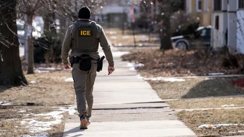 عميل من إدارة الهجرة والجمارك يسير في حي سكني، مع التركيز على عملية ترحيل المهاجرين المرتبطين بعصابة ترين دي أراغوا.