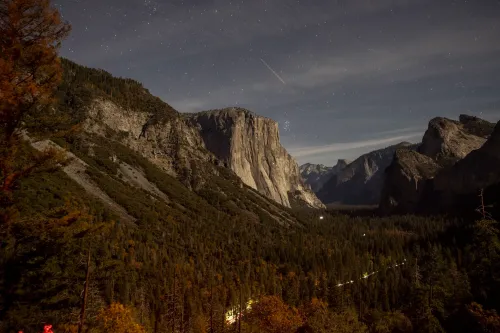 منظر ليلي لوادي Yosemite الوطني في كاليفورنيا يظهر الجبال والغابات تحت سماء مرصعة بالنجوم، مع تهديد مشروع طريق عقاري لحرمة المتنزه.