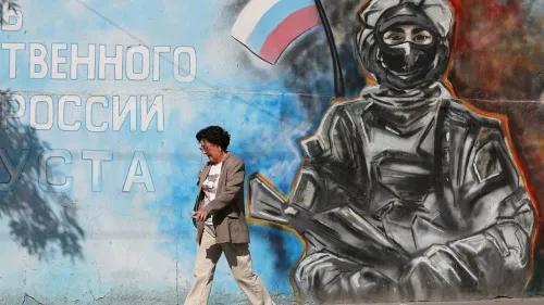 امرأة تسير بجوار جدارية تصور جنديًا يحمل سلاحًا، مع العلم الروسي في الخلفية، تعكس التوترات السياسية حول أوكرانيا.