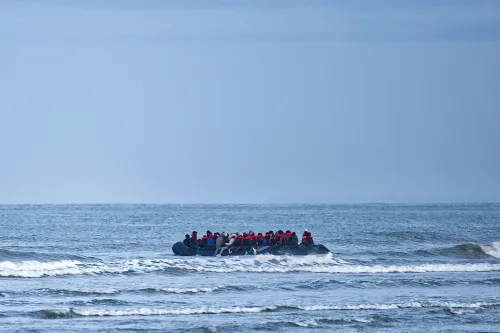 مجموعة من اللاجئين في قارب مطاطي في عرض البحر، تعبير عن تحديات الهجرة واللجوء في ظل السياسات الأمريكية الجديدة.