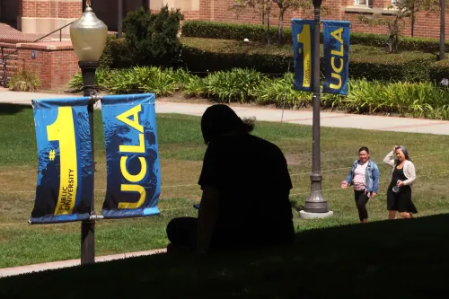شعار جامعة كاليفورنيا في لوس أنجلوس (UCLA) مع العلم الذي يحمل الرقم 1، بينما يظهر طلاب يمشون في الحرم الجامعي.