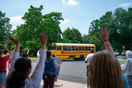 طلاب يلوحون بأيديهم لباخرة مدرسية صفراء أثناء مغادرتها، مما يعكس الحماس والارتباط بالمؤسسات التعليمية.