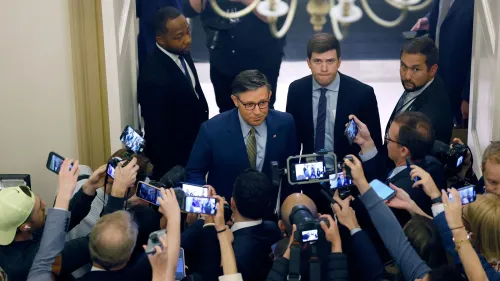 مجموعة من الصحفيين يحيطون بشخص يرتدي نظارات وقميصًا أزرق، في مشهد يعكس التوتر أثناء التصويت على مشروع قانون ترامب في مجلس النواب.