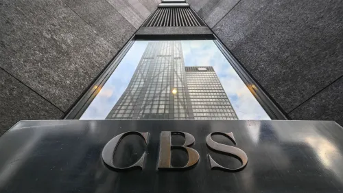 شعار CBS يظهر في المقدمة مع انعكاس مبنى مرتفع في الخلفية، مما يعكس سياق النزاع القانوني مع الرئيس ترامب.
