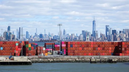 صورة لميناء يحتوي على حاويات شحن ملونة، مع skyline مدينة نيويورك في الخلفية، تعكس تأثير التعريفات الجمركية على التجارة.