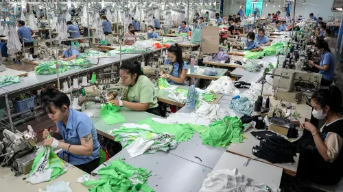 عاملات في مصنع خياطة في فيتنام، يركزن على العمل على الملابس، وسط بيئة مزدحمة وآلات خياطة، تعكس أهمية الشراكة التجارية مع الولايات المتحدة.