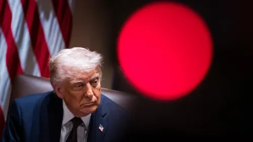 تظهر الصورة ترامب في اجتماع رسمي، مع خلفية تتضمن الأعلام الأمريكية. تعكس تعابير وجهه القلق بشأن قضايا الهجرة وتأثيرها على الطلاب الدوليين.