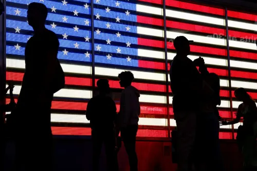 أشخاص يقفون في ظل علم الولايات المتحدة المضيء، مما يعكس النقاش حول الإحصاء السكاني وتأثيره على السياسة الأمريكية.