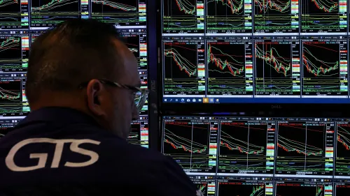 شخص يجلس أمام شاشات متعددة تعرض بيانات سوق الأسهم والرسوم البيانية، في بيئة تداول نشطة تعكس حالة عدم اليقين الاقتصادي.