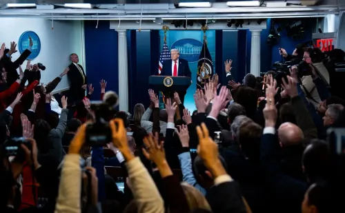 ترامب يتحدث في مؤتمر صحفي بالبيت الأبيض، محاطًا بالصحفيين الذين يرفعون أيديهم لطرح الأسئلة، مما يعكس التوترات الإعلامية.