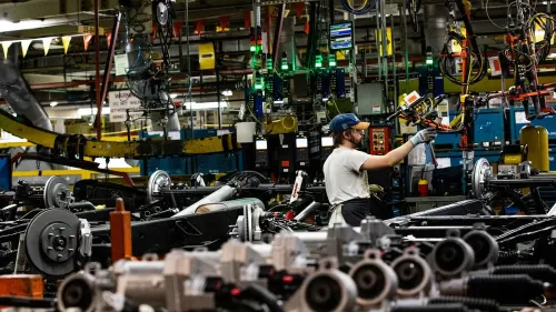 عامل في مصنع سيارات يعمل على تجميع أجزاء المركبات، مع وجود معدات وآلات في الخلفية، يعكس تأثير التعريفات الجمركية على الإنتاج.