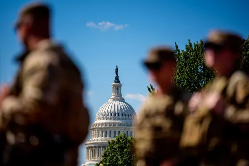 جنود يرتدون الزي العسكري يقفون في المقدمة، مع قبة مبنى الكابيتول الأمريكي في الخلفية، مما يعكس التوترات السياسية الحالية بين إدارة ترامب والكونغرس.