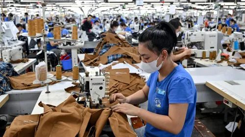 امرأة تعمل في مصنع للخياطة في فيتنام، محاطة بأقمشة ومواد، تعكس تأثير التجارة الدولية على أسعار السلع في الولايات المتحدة.