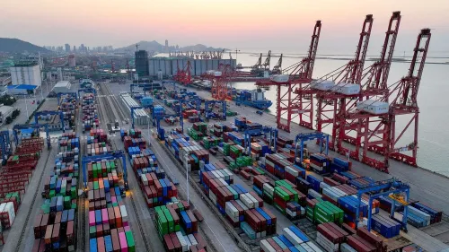 صورة لميناء يحتوي على حاويات شحن ملونة وأوناش تحميل، تعكس تأثير الحرب التجارية بين الولايات المتحدة والصين.