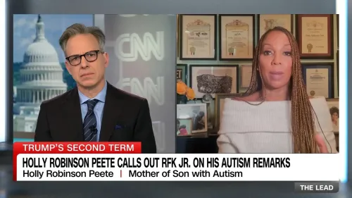 هولي روبنسون بيت تتحدث عن تصريحات روبرت كينيدي جونيور بشأن التوحد، بينما يظهر خلفها شهادات وجوائز، مع مبنى الكابيتول في الخلفية.