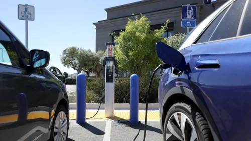 محطة شحن للسيارات الكهربائية تُظهر سيارتين متصلتين بالشاحن، مع لافتات توضح المنطقة المخصصة للسيارات الكهربائية.