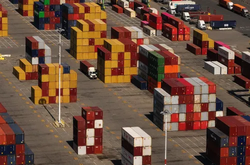 صورة لمستودع يحتوي على حاويات شحن ملونة مرتبة بشكل منظم، تعكس التغيرات في التعريفات الجمركية الأمريكية وتأثيرها على التجارة الدولية.