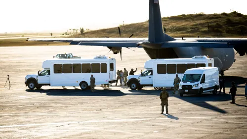 حافلات بيضاء تنتظر على مدرج قاعدة غوانتانامو البحرية، مع وجود جنود أمريكيين، في إطار جهود نقل المهاجرين.
