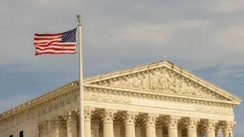 مبنى المحكمة العليا الأمريكية مع العلم الأمريكي يرفرف في المقدمة، مما يرمز إلى القضايا القانونية المتعلقة بسلطة الرئيس ترامب.