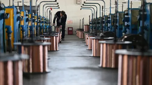 عامل في مصنع للنحاس يتفقد أسلاك النحاس الملفوفة، مع وجود آلات تصنيع في الخلفية، في سياق تأثير التعريفات الجمركية.