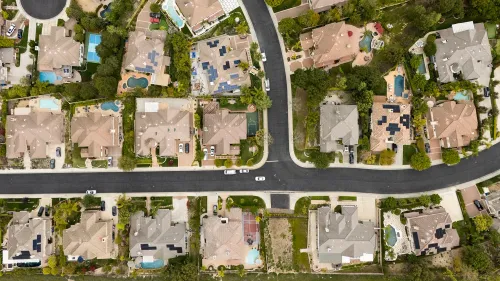 صورة جوية لحي سكني يضم منازل مع حدائق ومسابح، تعكس تأثير ارتفاع أسعار العقارات على ضرائب الأرباح الرأسمالية.