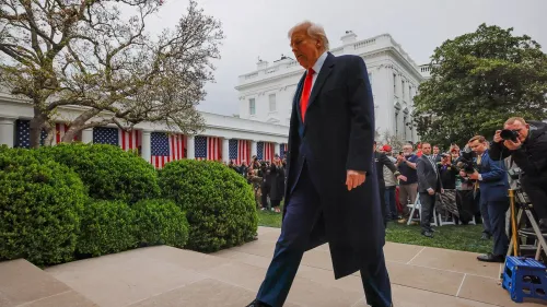 الرئيس ترامب يسير في حديقة البيت الأبيض، محاطًا بالمراسلين، بينما تبرز الأعلام الأمريكية خلفه، في أجواء من التوتر السياسي.