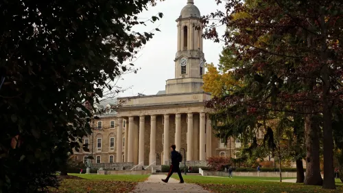 مبنى تعليمي كبير مع أعمدة، حيث يسير طالب في الحرم الجامعي. تعكس الصورة التغييرات في إدارة قروض الطلاب وتأثيرها على التعليم.