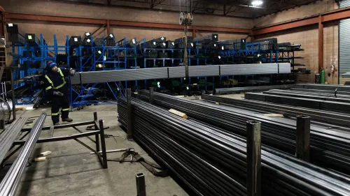 عامل يعمل في منشأة لتخزين الصلب والألومنيوم، وسط صفوف من القضبان المعدنية، في سياق الرسوم الجمركية التي فرضها ترامب.