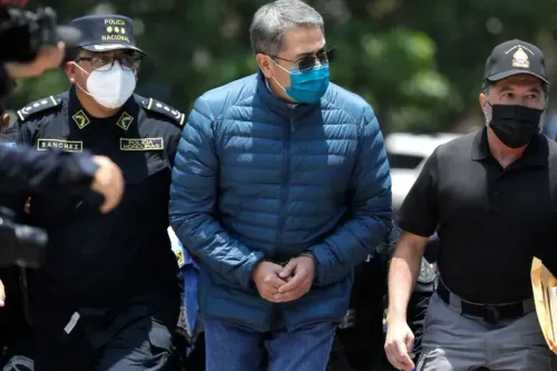 رئيس هندوراس السابق خوان أورلاندو هيرنانديز محاطاً برجال الشرطة، مع التركيز على ملابسه الزرقاء وقناع الوجه، في سياق قضايا الاتجار بالمخدرات.