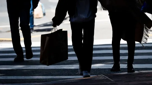 مجموعة من الأشخاص يسيرون عبر ممر مشاة، يحمل أحدهم حقيبة تسوق، مما يعكس النشاط الاقتصادي والإنفاق في ظل المخاوف من الركود.