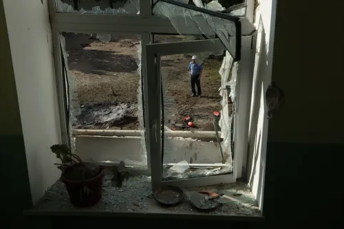 من خلال نافذة مكسورة، يظهر رجل يقف في الخارج بين حطام، مما يعكس آثار الحرب في أوكرانيا وتداعياتها الإنسانية.
