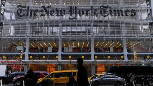 مبنى صحيفة نيويورك تايمز في نيويورك، مع لافتة كبيرة تحمل اسم الصحيفة، بينما يمر الناس والسيارات في الشارع.