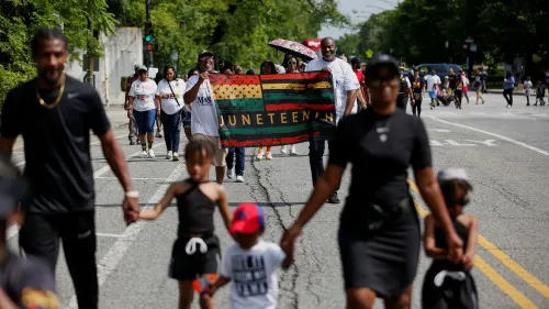 محتفلون يحملون علم يوم جونيتنث خلال مسيرة في الشارع، يعبرون عن الفخر والاحتفال بذكرى تحرير العبيد في الولايات المتحدة.