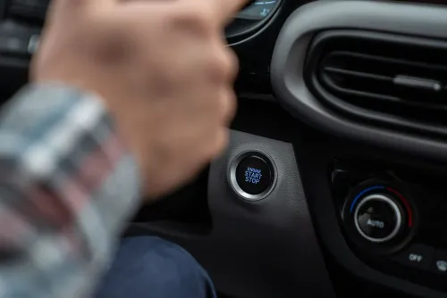 زر تشغيل وإيقاف المحرك في سيارة حديثة، مع يد شخص تلمسه. الصورة تعكس التغييرات المحتملة في تقنيات السيارات بعد إلغاء لوائح انبعاثات السيارات.