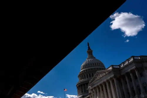 صورة لمبنى الكابيتول الأمريكي تحت سماء زرقاء مع سحابة بيضاء، تعكس تأثير الإغلاق الحكومي على الاقتصاد والسياسة النقدية.