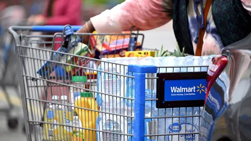 عربة تسوق مليئة بالمنتجات الغذائية والمشروبات، تحمل علامة وول مارت، تعكس تأثير التعريفات الجمركية على الأسعار.