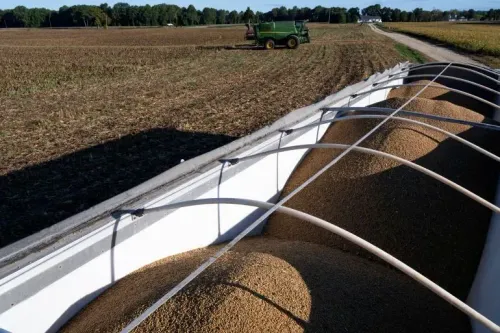 حمولة من حبوب فول الصويا في شاحنة على مزرعة، مع جرار زراعي يعمل في الخلفية، تعكس تأثير السياسات التجارية على الزراعة الأمريكية.