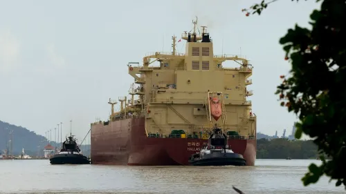 سفينة كبيرة تعبر قناة بنما، مع قوارب مساعدة تقترب منها، مما يعكس أهمية القناة في التجارة العالمية.