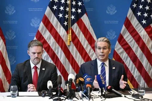 اجتماع رسمي يتحدث فيه مسؤول أمريكي وسط أعلام الولايات المتحدة، مع وجود ميكروفونات متعددة، حيث يناقش تأثير الحرب التجارية مع الصين.