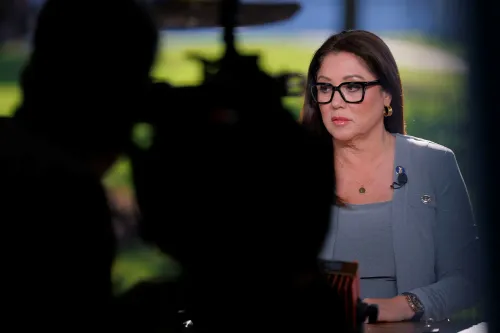 امرأة ترتدي نظارات وتظهر بملامح جادة خلال مقابلة، مع خلفية ضبابية. تعكس الصورة الأجواء السياسية المتوترة حول الاقتصاد.