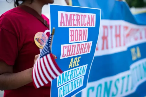 لافتة تحمل شعارات تدعم حق المواطنة بالميلاد للأطفال المولودين في الولايات المتحدة، مع علم أمريكي صغير.