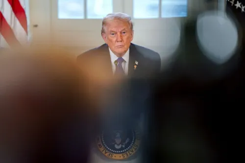 ترامب يجلس في غرفة رسمية، مع تعبير وجه جاد، بينما تبرز خلفه الأعلام الأمريكية. تعكس الصورة توتر الوضع السياسي الحالي.