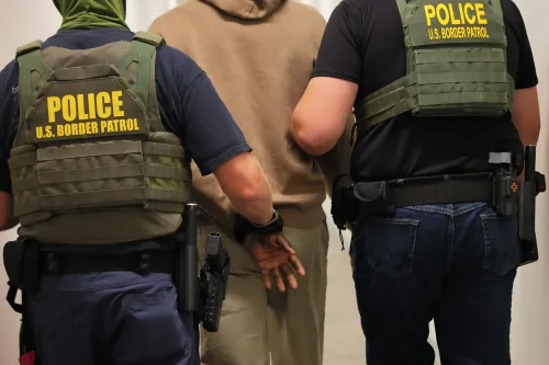 اعتقال شخص من قبل عناصر من دوريات الحدود الأمريكية، يرتديان سترات واقية مكتوب عليها "شرطة".